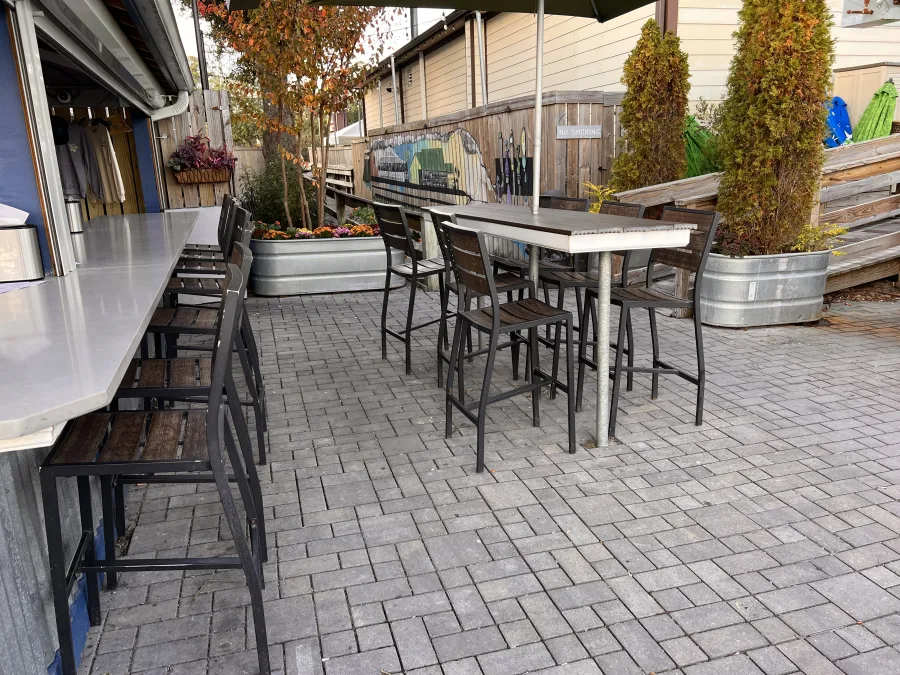 An empty bar patio on the boardwalk in the morning, stools pushed in and planters out