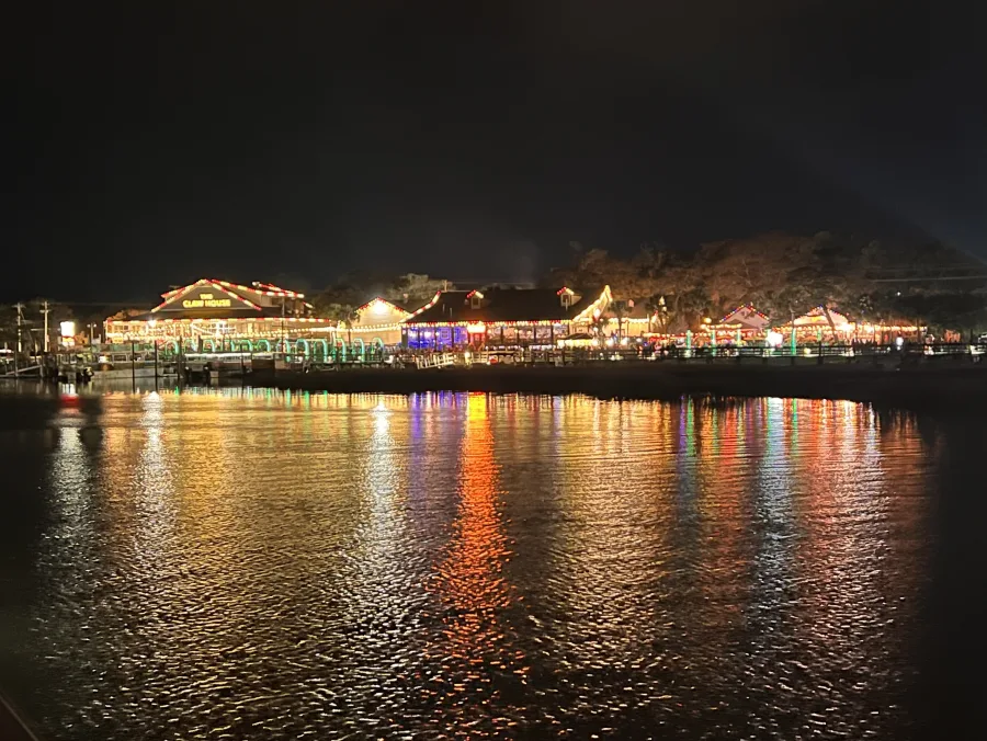 The Murrells Inlet MarshWalk after dark seen from across the creek, restaurant lights running the length of the boardwalk and reflecting on the water